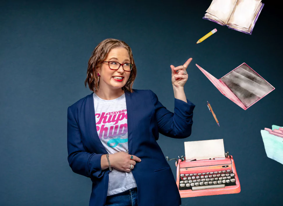 ALT text for accessibility: The image captures Anastasia from No Grey Suits smiling and pointing upwards, set against a dark blue backdrop. She is fashionably attired in a blazer over a "Chupa Chups" t-shirt. Floating whimsically around her are a pencil, a stack of books, an open notebook, and a vibrant red typewriter, hinting at a creative or literary environment. The composition conveys a sense of creativity and a playful approach to work.